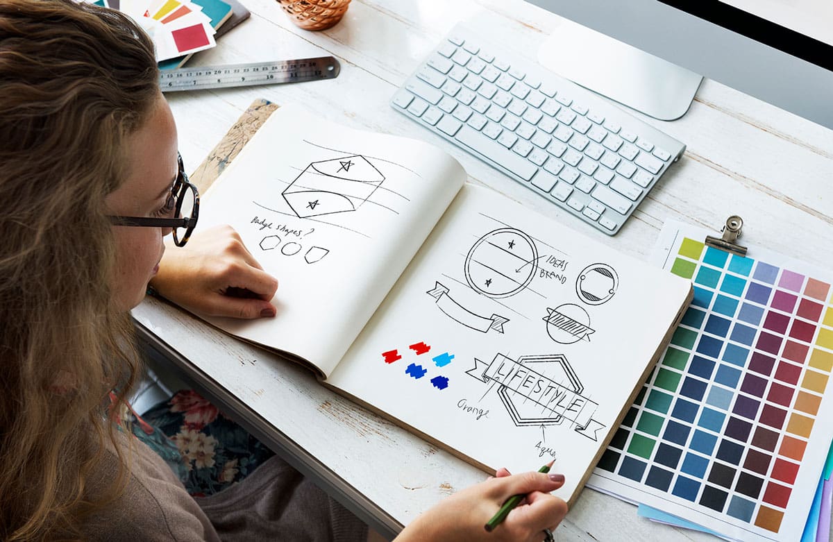 Graphic designer sketching brand identity concepts and logo ideas with color palette samples on desk
