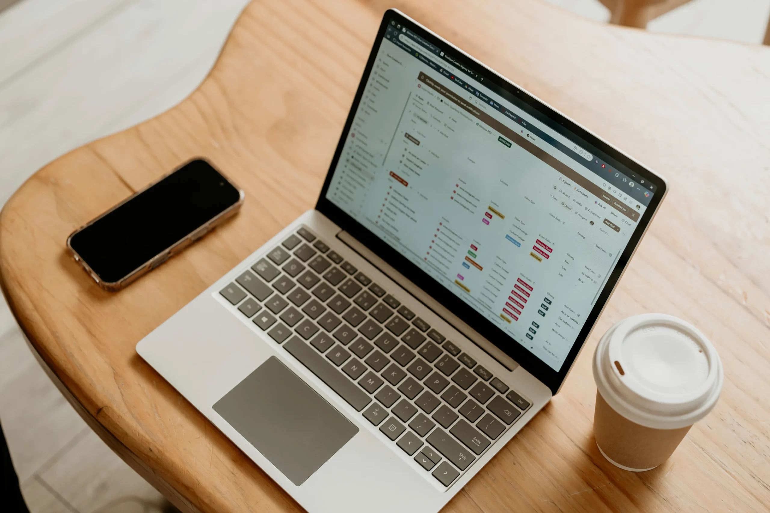 Laptop displaying project management dashboard on a wooden table with phone and coffee
