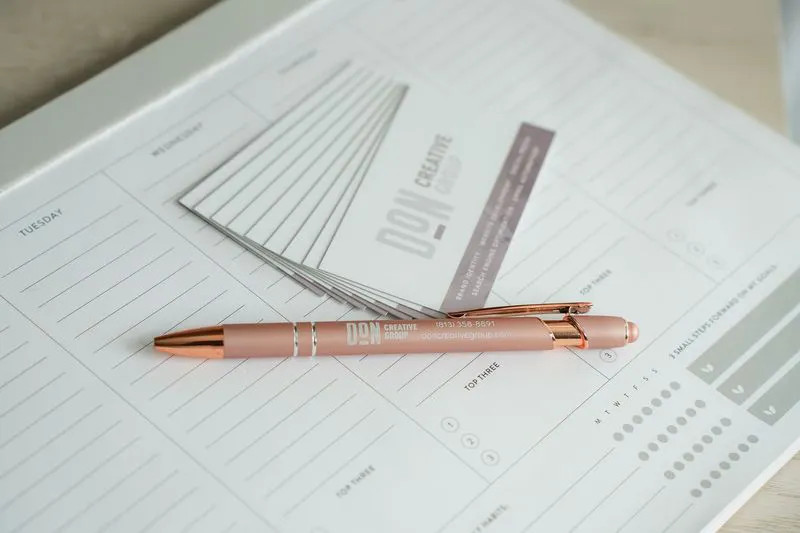 Don Creative Group branded pen and business cards placed on a weekly planner workspace