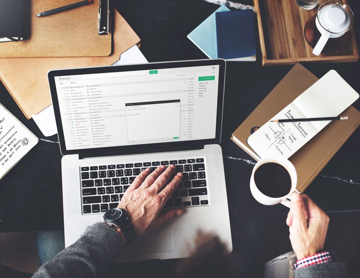 Person working on email marketing strategy at a desk with a laptop, coffee, and notes on branding and audience research.