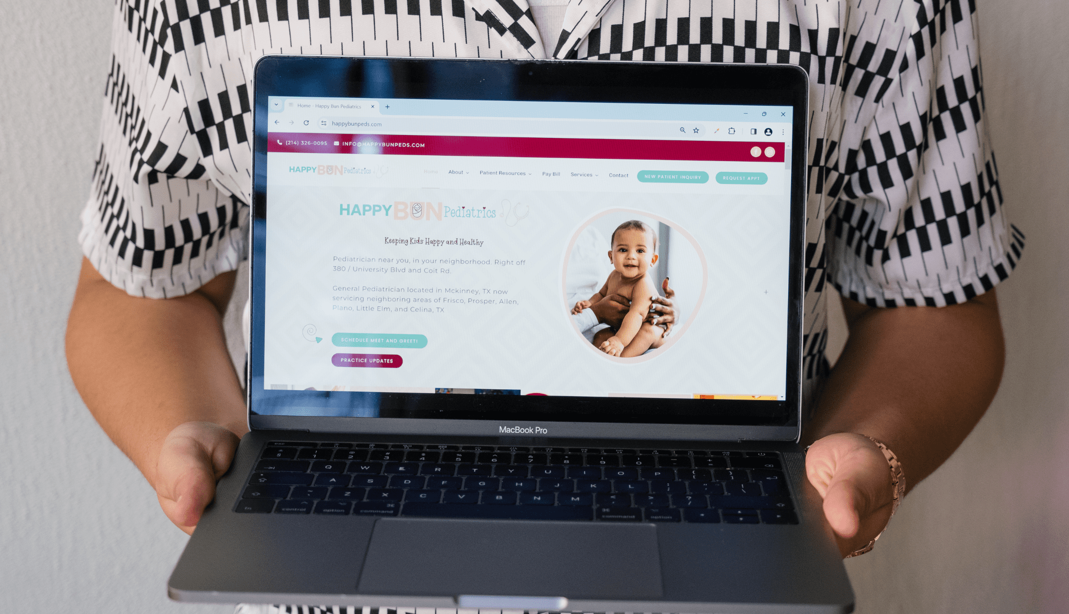 Person holding a MacBook Pro displaying the Happy Bun Pediatrics website, featuring a smiling baby and service locations in Texas.