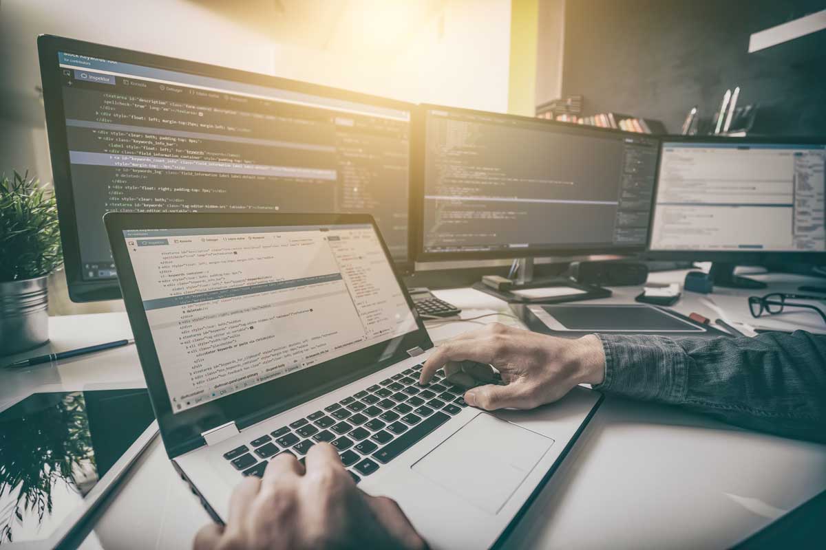 Developer working on a laptop with multiple monitors displaying website code